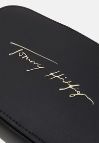 Custodia in pelle nera con logo in oro, texture liscia e dettagli di cucitura sottili. Design compatto e rettangolare.