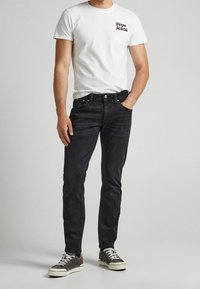 Bílá tričko s logem "Pepe Jeans", tmavé denimové džíny, šedé boty s bílou podrážkou a ležérní střih. Jednoduchý, čistý design.