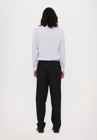 Hellblau gestreiftes Hemd und schwarze Hosen in lässiger Passform. Das Hemd hat lange Ärmel und die Hose verfügt über zwei Gesäßtaschen.
