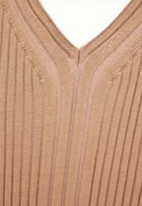 Beige ribbed Strick-Top mit V-Ausschnitt und definierten vertikalen Streifen; die texturierte Detailgestaltung ist an Ausschnitt und Kanten gut sichtbar.