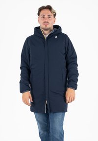 Marineblauwe gevoerde jas met een capuchon, voorzien van een rits, elastische manchetten en een klein logo op de borst. Textuurstof met een gladde afwerking.
