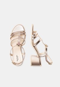 Sandali dorati con cinturino alla caviglia, dotati di dettagli in metallo testurizzato e tacco a blocco. Sottopiede morbido e design elegante.