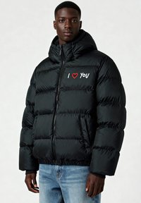 Doudoune noire avec fermeture éclair à l'avant, capuche et poignets élastiques. Présente un texte blanc et rouge "I ❤️ YOU" sur le côté gauche de la poitrine.