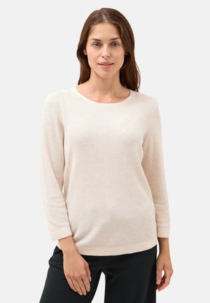 Maglione lavorato a maglia beige chiaro a maniche lunghe con scollo rotondo e motivo testurizzato, abbinato a pantaloni neri. Silhouette aderente ma rilassata.