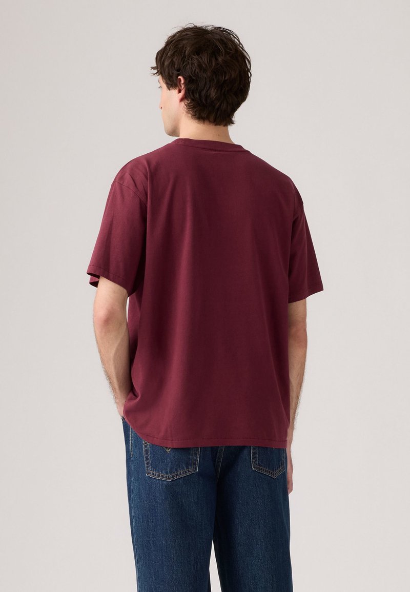 Burgunderfarbene Baumwoll-T-Shirt mit kurzen Ärmeln und entspannter Passform, kombiniert mit blauen Jeans. Hat einen Rundhalsausschnitt und ein minimalistisches Design.