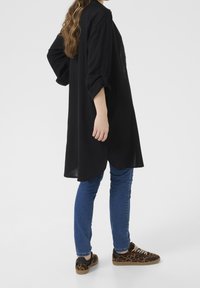 Czarna sukienka koszulowa z podwiniętymi rękawami, zaokrąglonym dołem, w połączeniu z niebieskimi dżinsami i trampkami w panterkę z sznurówkami oraz gumową podeszwą.