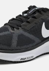 Black athletic shoe featuring a breathable mesh upper with gray stripes, black laces, and a white logo; Zoom cushioning visible on the sole.
