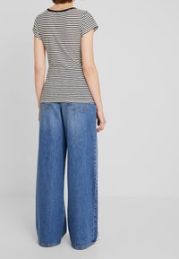 Striped black and white short-sleeve shirt paired with wide-leg light blue denim jeans. The shirt has a round neckline and the jeans have back pockets.