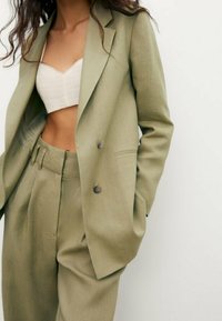 Light olive green tailored blazer with double buttons, paired with matching high-waisted trousers. Smooth, textured fabric with subtle sheen.