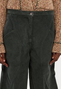 Mørkegrønne kordfløjlsbukser med vide ben, der har ribbet tekstur, frontlukning med knap og skrå syninger for et skræddersyet look.
