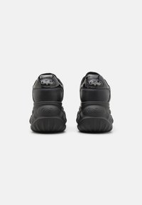 Black sneakers with a glossy leather upper, padded collar, and textured rubber sole featuring a distinct wavy pattern. Logo on heel.