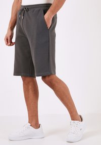 Grå, knælange shorts lavet af tekstureret stof, med en elastisk talje med snøring og sidelommer. Kombinationen med hvide sneakers.