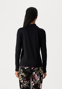 Schwarzes Langarmoberteil mit einem Rollkragen, figurbetontem Design und glatter Textur, kombiniert mit gemusterten schwarzen Blumenhosen. Die Rückansicht zeigt minimale Details.
