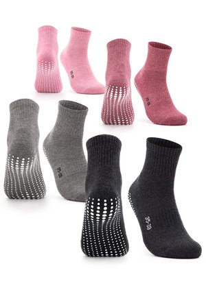 Feet wearing maroon grip socks with white rubber dots on soles and black leggings with ribbed texture, against a white background.