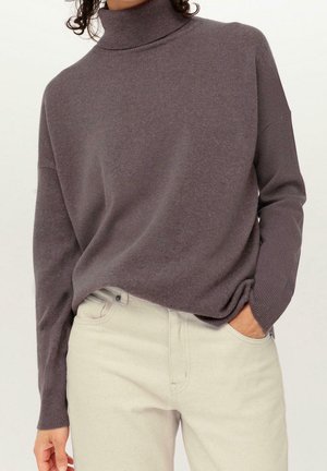 Suéter de cuello alto gris hecho de un suave tejido de punto. Presenta un corte holgado y un cuello acanalado. Combinado con unos vaqueros de color claro.