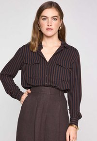 Camicia a righe con bottoni, in blu scuro e ruggine, con colletto, due tasche anteriori e maniche lunghe, abbinata a pantaloni scuri a vita alta.
