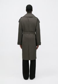 Khaki trench coat with a belt, double-breasted front, and wide notched collar. Features long sleeves and a straight cut.