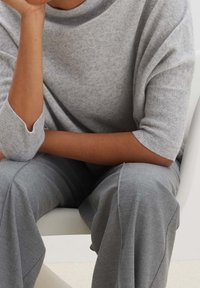 Světle šedý, měkký pletený svetr s krátkými rukávy; v kombinaci s odpovídajícími šedými širokými kalhotami. Hladká textura, uvolněný střih, minimalistický design.