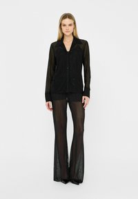 Chemise noire transparente à boutons avec des manches longues et un col pointu, associée à un pantalon évasé transparent assorti à motifs verticaux.