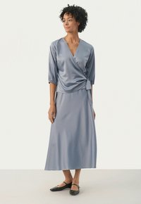 Sateen wrap dress vaale sinisellä värillä, kolmivartiset hihat, sidottu vyötärölle. Lattiapituinen hame, sileä rakenne. Mustat ballet-lenkkarit täydentävät asua.