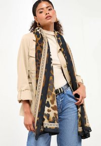 Fular cu imprimeu de leopard în nuanțe de negru și bej, având o margine geometrică. Material ușor și moale care se așază elegant pe purtător.