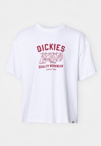 T-shirt in cotone bianco con una stampa grafica rossa che presenta il testo "DICKIES" e "QUALITY WORKWEAR", enfatizzando il design casual e la vestibilità oversize.