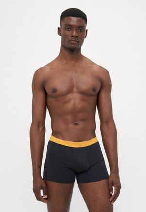 Schwarze Baumwoll-Boxershorts mit einem gelben elastischen Bund. Glatte Textur und enganliegende Form, entworfen für Komfort und Unterstützung.