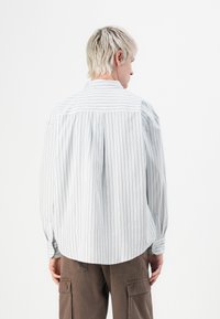 Person with short blonde hair wearing a white long-sleeve shirt with thin vertical stripes and brown cargo pants, facing away.