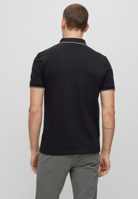 Czarna koszulka polo z krótkim rękawem, z klasycznym kołnierzykiem, białą lamówką przy kołnierzyku i rękawach, wykonana z gładkiego materiału, o minimalistycznym designie.