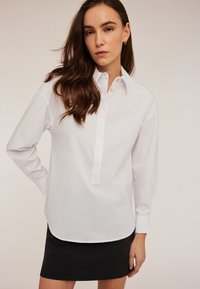Witte langemouwen shirt met een knoopsluiting en kraag, gemaakt van gladde stof, gecombineerd met een aansluitende zwarte rok.