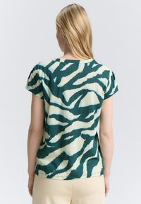 T-shirt vert et crème à manches courtes avec un design à motifs comprenant des rayures abstraites ondulées. Fabriqué en tissu doux avec une coupe décontractée.