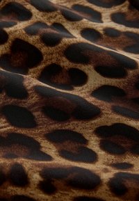 Loomade mustriga kangas, millel on beež taust ja suured, ebaregulaarsed mustad ning tumepruunid laigud. Materjalil on sile tekstuur.