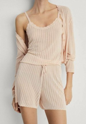 Světle růžová pletená souprava na volný čas, která zahrnuje top bez rukávů s vlnitým okrajem a odpovídající šortky na šňůrku, obě s vertikálním žebrováním.