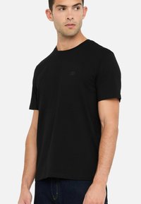 T-shirt nera a maniche corte con scollatura rotonda e un logo discreto sul petto. Realizzata in morbido cotone con una texture liscia.