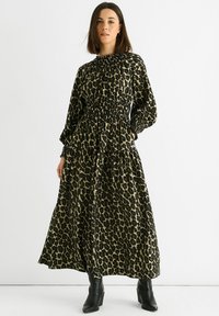 Maxi dress in green and black leopard print, featuring a smocked waist, long sleeves, and a tiered skirt. Paired with black ankle boots.