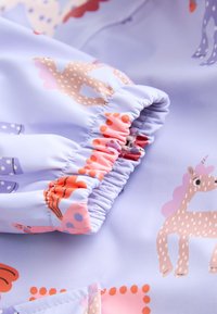 Manche en tissu violet clair avec poignet élastique, décorée de motifs licorne rose et beige et de pois.