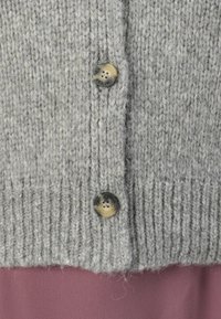 Cardigan grigio a maglia con due bottoni, texture a coste e finitura morbida. Sotto, è parzialmente visibile un indumento a strati rosa.