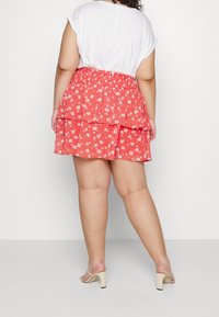 Red floral tiered skirt with a smocked waistband, made from lightweight fabric, layered design, and a ruffled hem. Paired with beige heels.