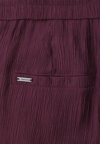 Tissu texturé violet foncé avec une ceinture élastique et une poche horizontale étiquetée "Street One" cousue près du centre supérieur.