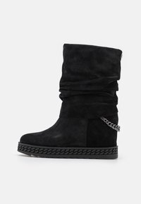 Černé kotníkové boty z semiše s povislým designem, zdobené řetízkovým detailem a texturovanou černou podrážkou s vyplétaným vzorem.
