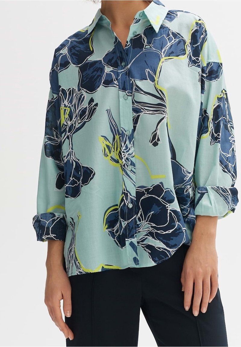 Light blue button-up shirt with a floral pattern in navy and yellow. Features a collar and rolled sleeves, made from a smooth fabric.