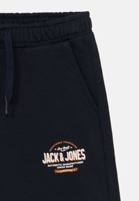 Tumši zili sporta bikses ar elastīgu jostasvietu, stiepjamu auklu un sānu kabatu. Ar oranžu un baltu logo izšuvumu. Mīksta kokvilnas maisījuma audums.