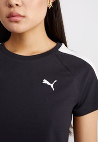 Juodas marškinėliai su baltais pečių akcentais, su mažu baltu Puma logotipu ant krūtinės, pagaminti iš lygios medžiagos.