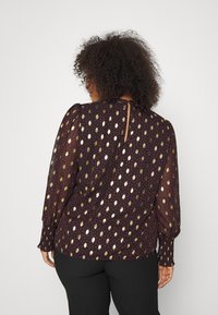 Blusa trasparente a maniche lunghe in marrone scuro con motivo metallico dorato e bacca, con polsini arricciati e dettaglio a occhio di chiave sul retro.