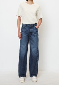 Light beige short-sleeve t-shirt paired with dark blue wide-leg jeans, featuring a classic five-pocket design and a slight wash effect.