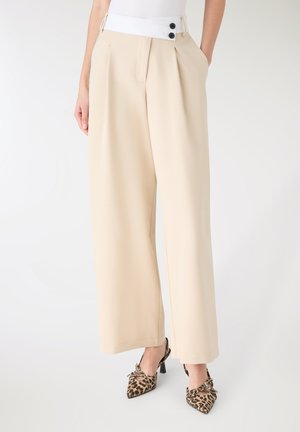 Pantaloni beige a gamba larga con una cintura bianca caratterizzata da due bottoni neri, texture liscia e caduta significativa.