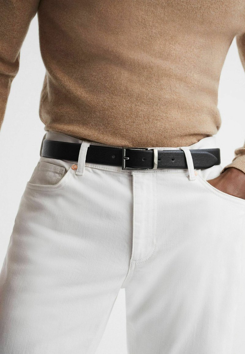Vita denimjeans med en figursydd design, ihop med ett svart läderbälte med en silverspänne, bärs med en brun tröja.