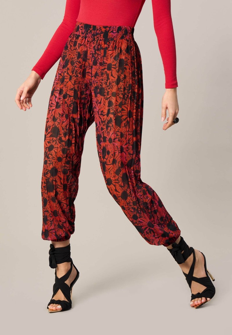 Pantalon à motif floral rouge et noir avec une taille élastique, des poignets resserrés et un tissu léger, associé à des talons noirs à brides.