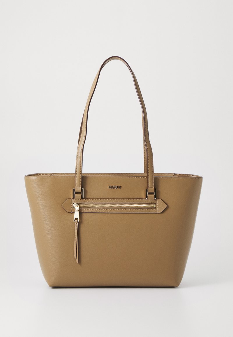 Barna műbőr tote táska cipzáras elülső zsebével, dupla fogantyúkkal és sima felülettel. DKNY logóval és ferde díszítésekkel rendelkezik.