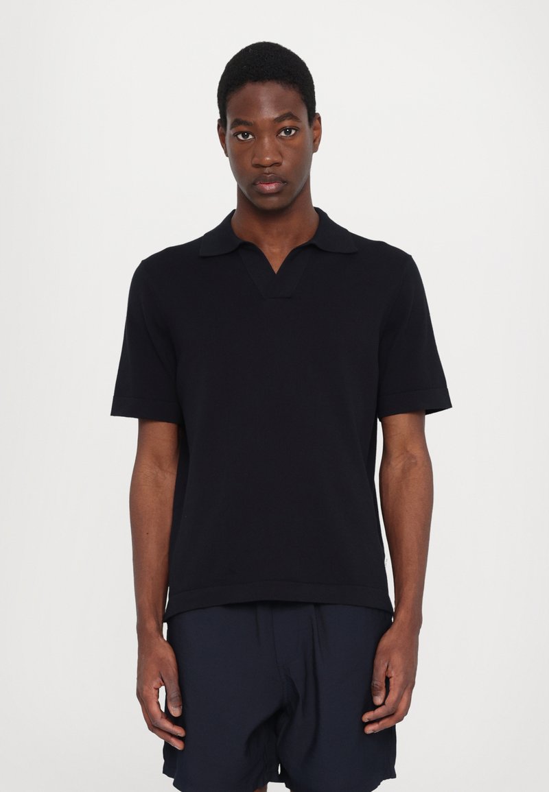 Polo preto de manga curta com decote em V e gola dobrada. Textura suave, design justo, usado com calções escuros. Simples e minimalista.